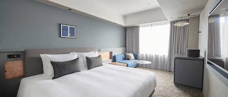A hotel room with a large bed, a small desk, a sofa, and a window with curtains.