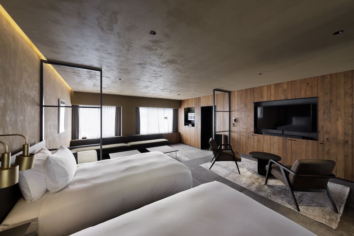 Une chambre d’hôtel moderne dotée d’un grand lit, d’un coin salon, d’un téléviseur fixé au mur et d’une grande fenêtre laissant entrer la lumière naturelle.