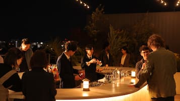 A bar area with a curved counter, illuminated by string lights, surrounded by guests.
