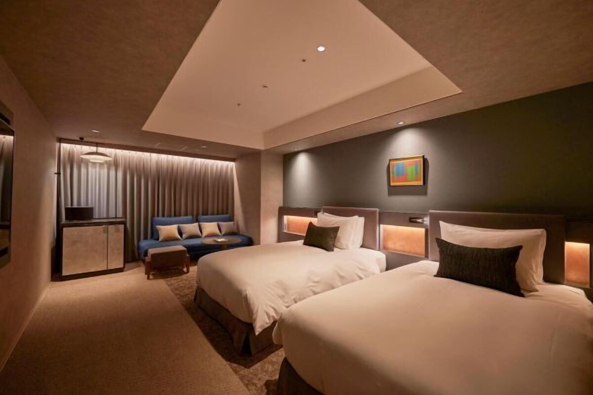 A hotel room with two beds, a sofa, a small table, and a painting on the wall.