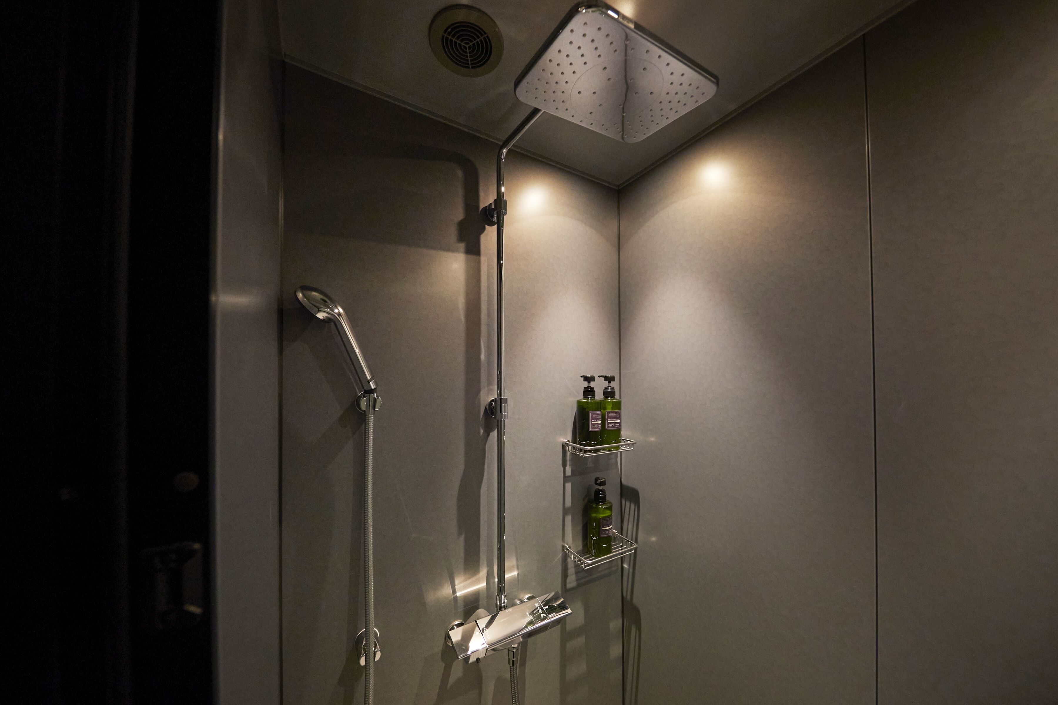 A modern shower with a handheld showerhead, a wall-mounted faucet, and a shelf with toiletries.