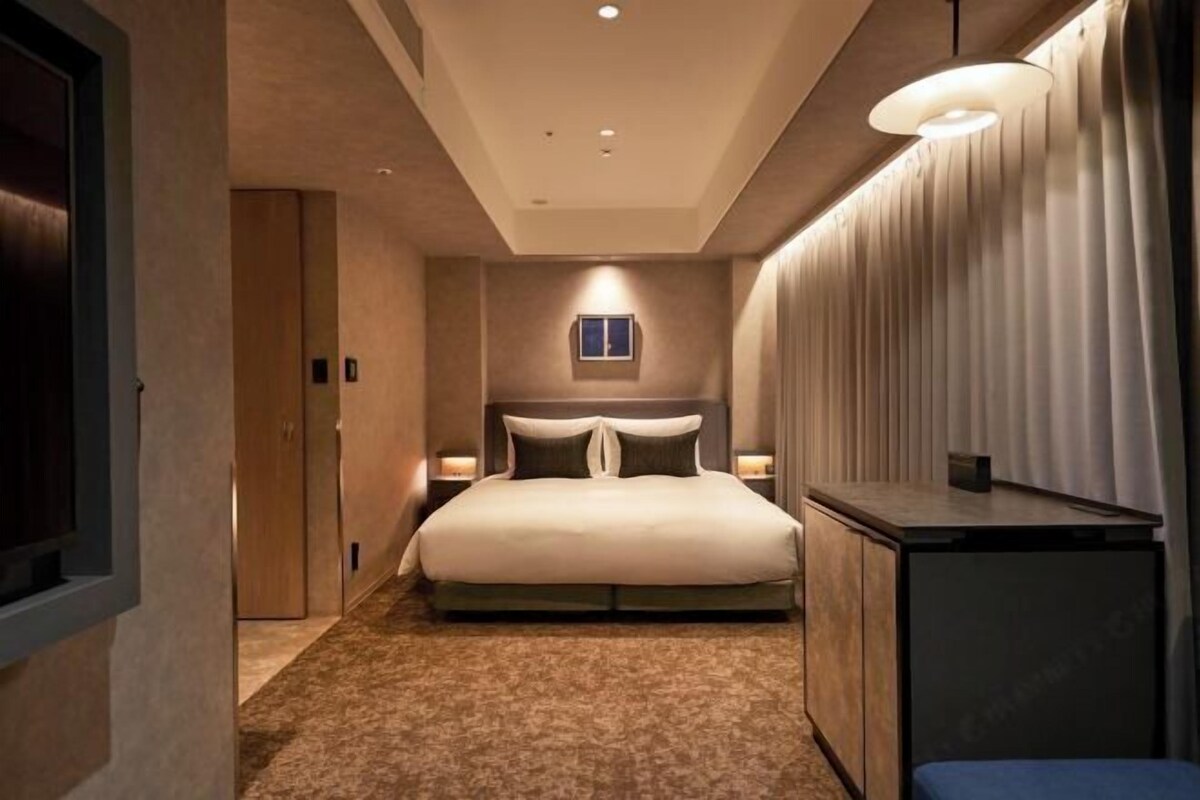 A bedroom with a bed, bedside tables, a nightstand, a desk, and a window.