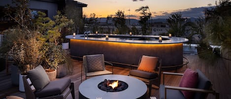 A modern outdoor seating area with a circular fire pit, lounge chairs, and ambient string lights.