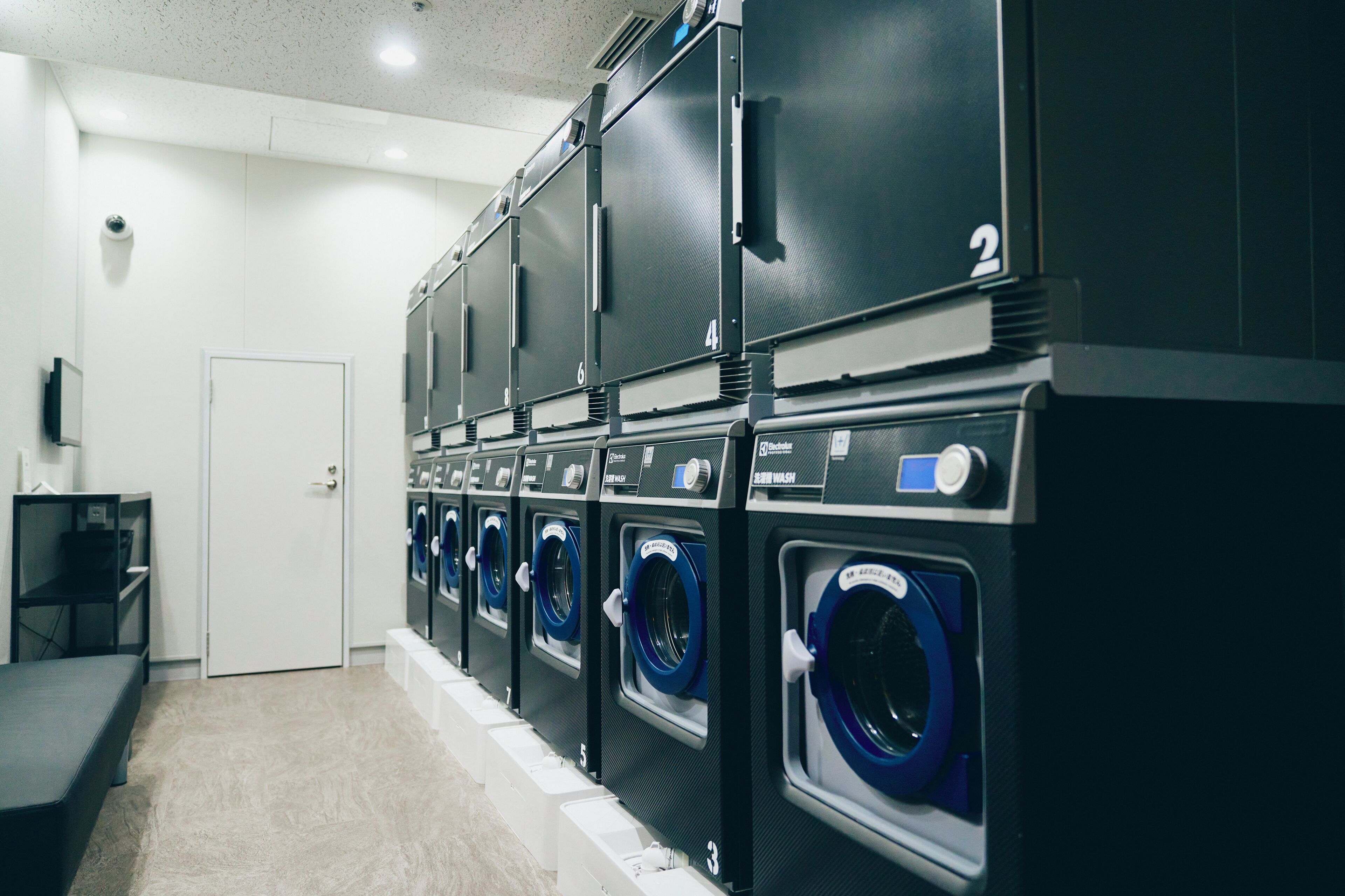 A laundry facility with multiple washing machines and dryers, a bench, and a door.