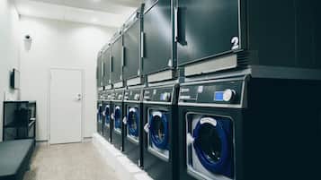 A laundry facility with multiple washing machines and dryers, a bench, and a door.