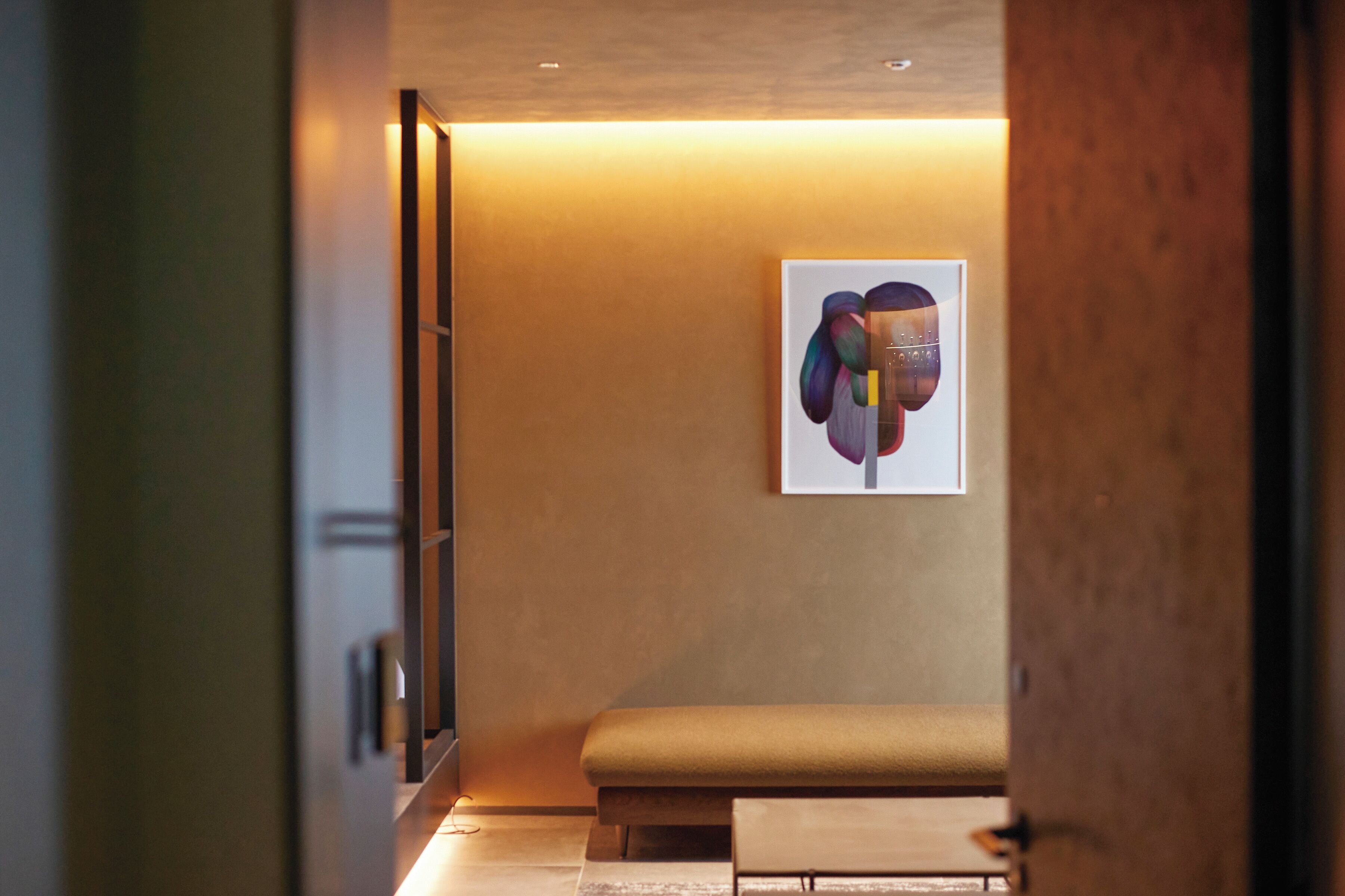 Un couloir avec un banc, une porte et une œuvre d’art encadrée accrochée au mur.