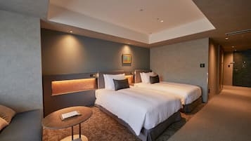 A modern hotel room with two beds, a small round table, and a headboard with built-in lighting.