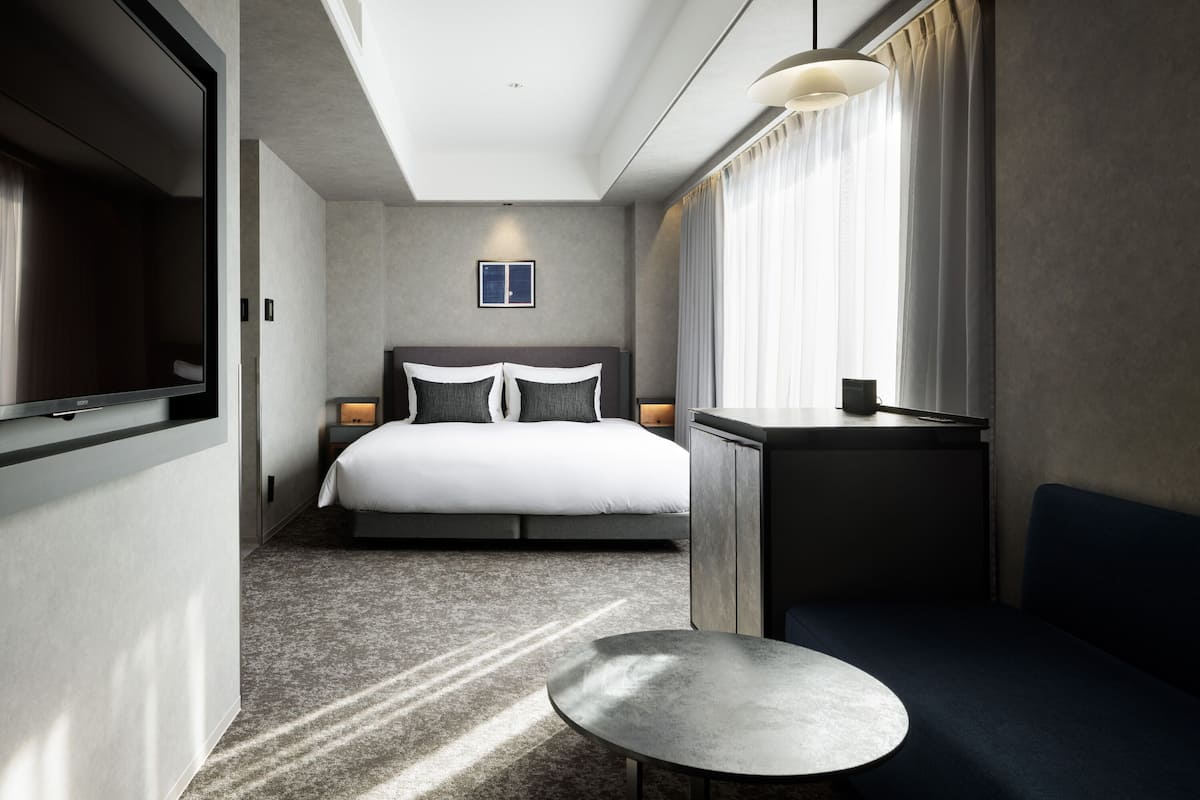 Une chambre d’hôtel moderne avec un grand lit, une petite table, une télévision et une fenêtre avec des rideaux.