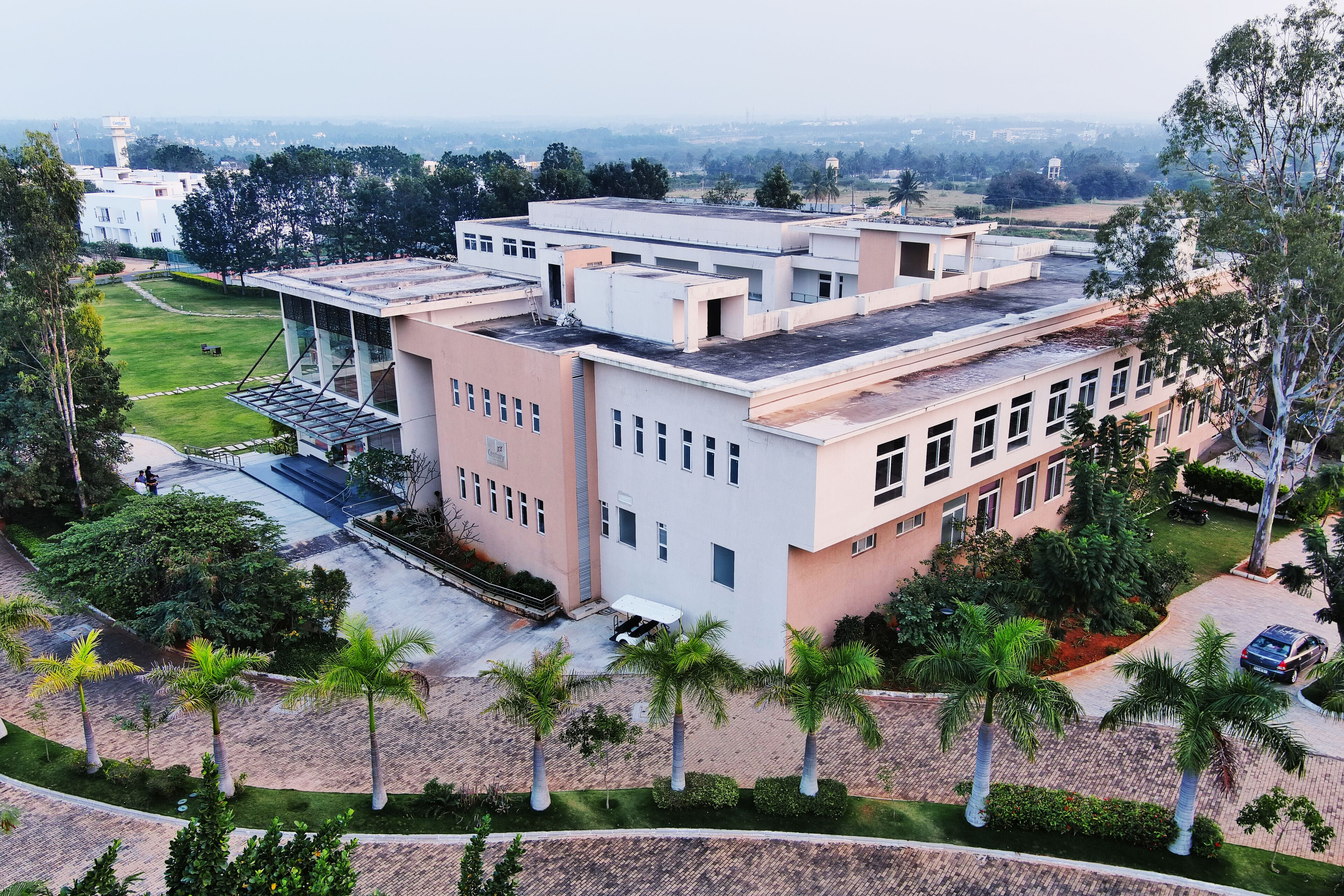 A multi-story building with a flat roof, surrounded by palm trees and a grassy area.