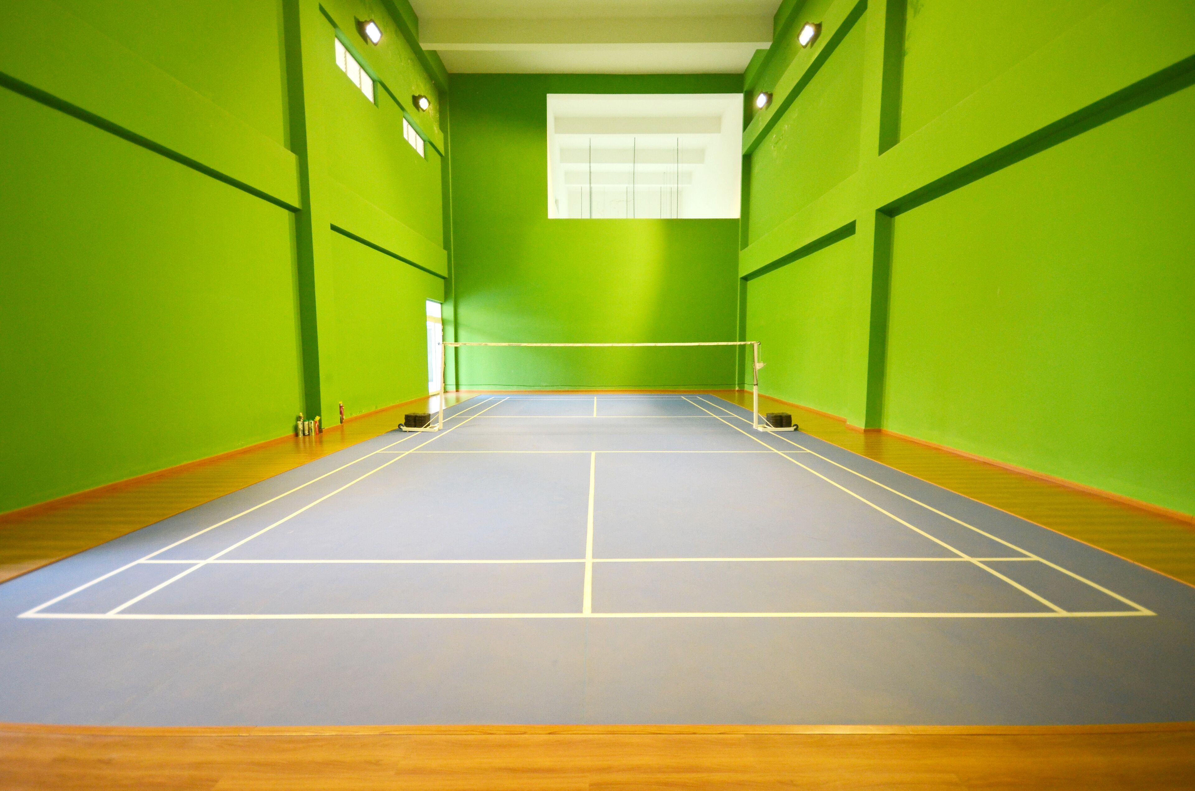 Pista de squash com paredes verdes, piso de madeira e uma rede no centro.