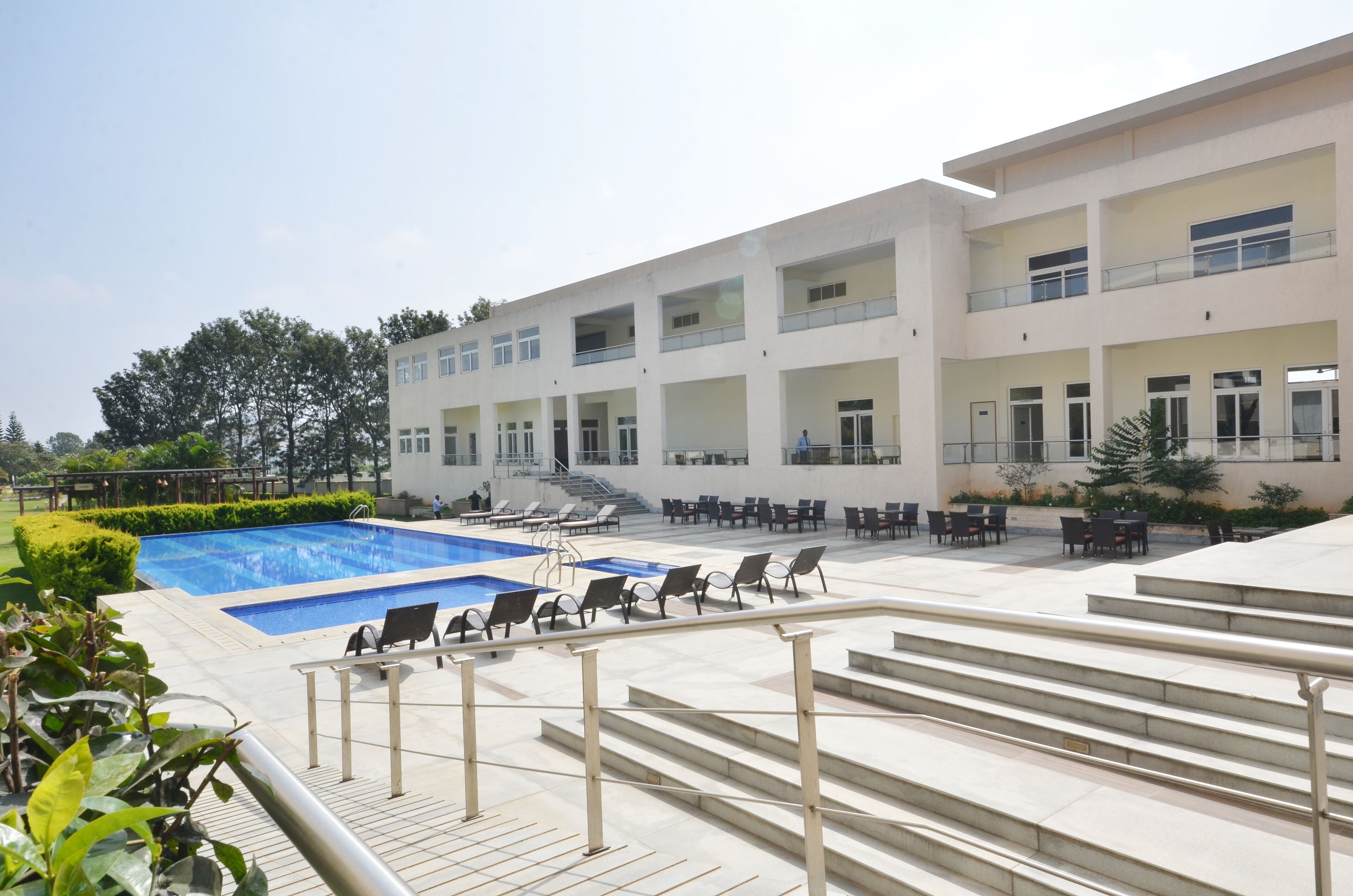 Un edificio moderno con piscina, mobiliario exterior y una escalera que lleva a los pisos superiores.