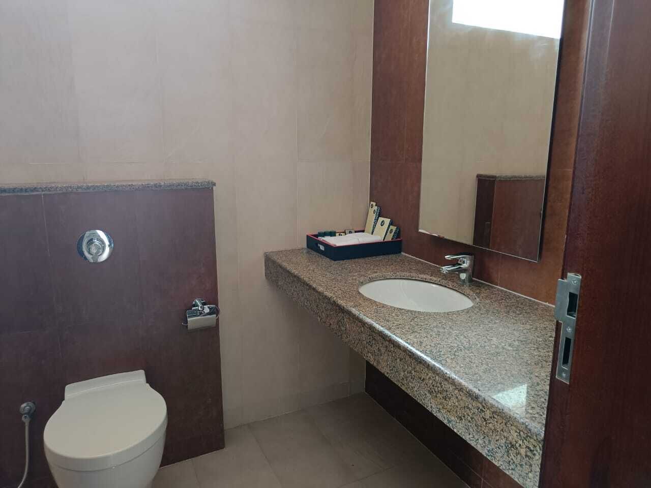 Un baño con inodoro blanco, lavabo de granito y espejo sobre el lavabo.
