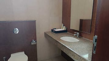 Un baño con inodoro blanco, lavabo de granito y espejo sobre el lavabo.