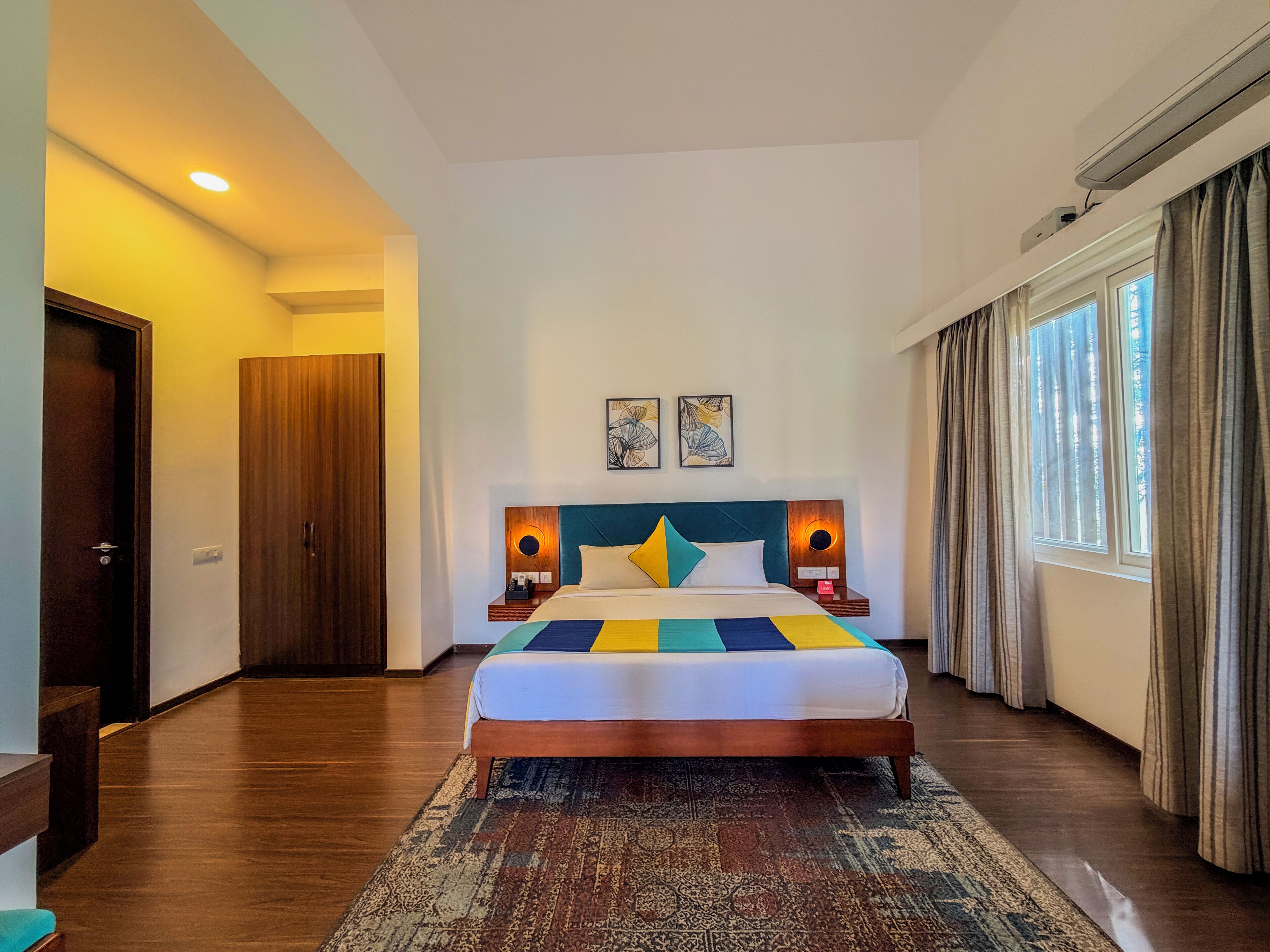 A hotel room with a wooden bed, a patterned rug, a nightstand with a phone, and a window with curtains.