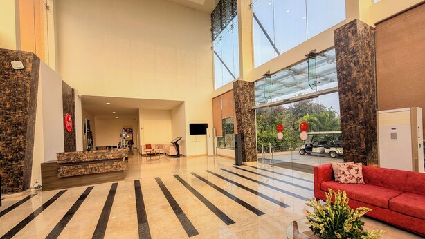 Un hall d’entrée spacieux comprenant un comptoir d’accueil, un canapé rouge, une table basse en verre et une grande fenêtre donnant sur l’extérieur.