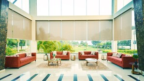 Un hall d’entrée spacieux au design moderne, comprenant un grand espace salon avec des canapés rouges et une table basse centrale, ainsi que de grandes fenêtres offrant une vue sur la verdure environnante.