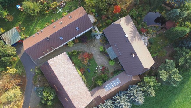 Ett flygbildsbild av ett bostadsområde med två hus, en liten damm och omgivande grönska.