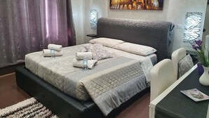 Ein Hotelzimmer mit Bett, Schreibtisch, Sessel und einem Gemälde des Kolosseums, sowie einem Vorhang.