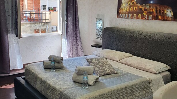 Ein modernes Hotelzimmer mit einem großen Bett, einem flachbildfernseher darüber und Blick auf ein Gebäude durch das Fenster.