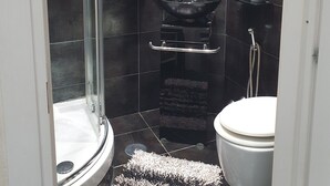 Ein kleines Badezimmer mit einer Duschkabine aus Glas, einer weißen Toilette, einem schwarzen Waschbecken mit Armatur und einem kleinen Spiegel darüber.
