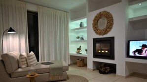 A modern living room with a sofa, a coffee table, a fireplace, shelves with decorative items, and a television. - Villa Vitabel 3 Bedroom with Infinity Pool and Sea View in Lindos (Lindos)