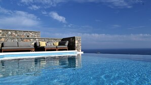 A infinity pool with a stone wall and a sofa with cushions. - Villa Vitabel 3 Bedroom with Infinity Pool and Sea View in Lindos (Lindos)
