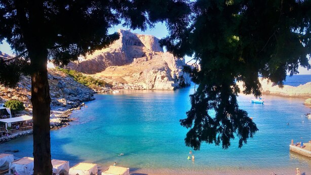 A coastal area with clear blue waters, a rocky cliff, and a beach with thatched umbrellas and lounge chairs. - Villa Vitabel 3 Bedroom with Infinity Pool and Sea View in Lindos (Lindos)