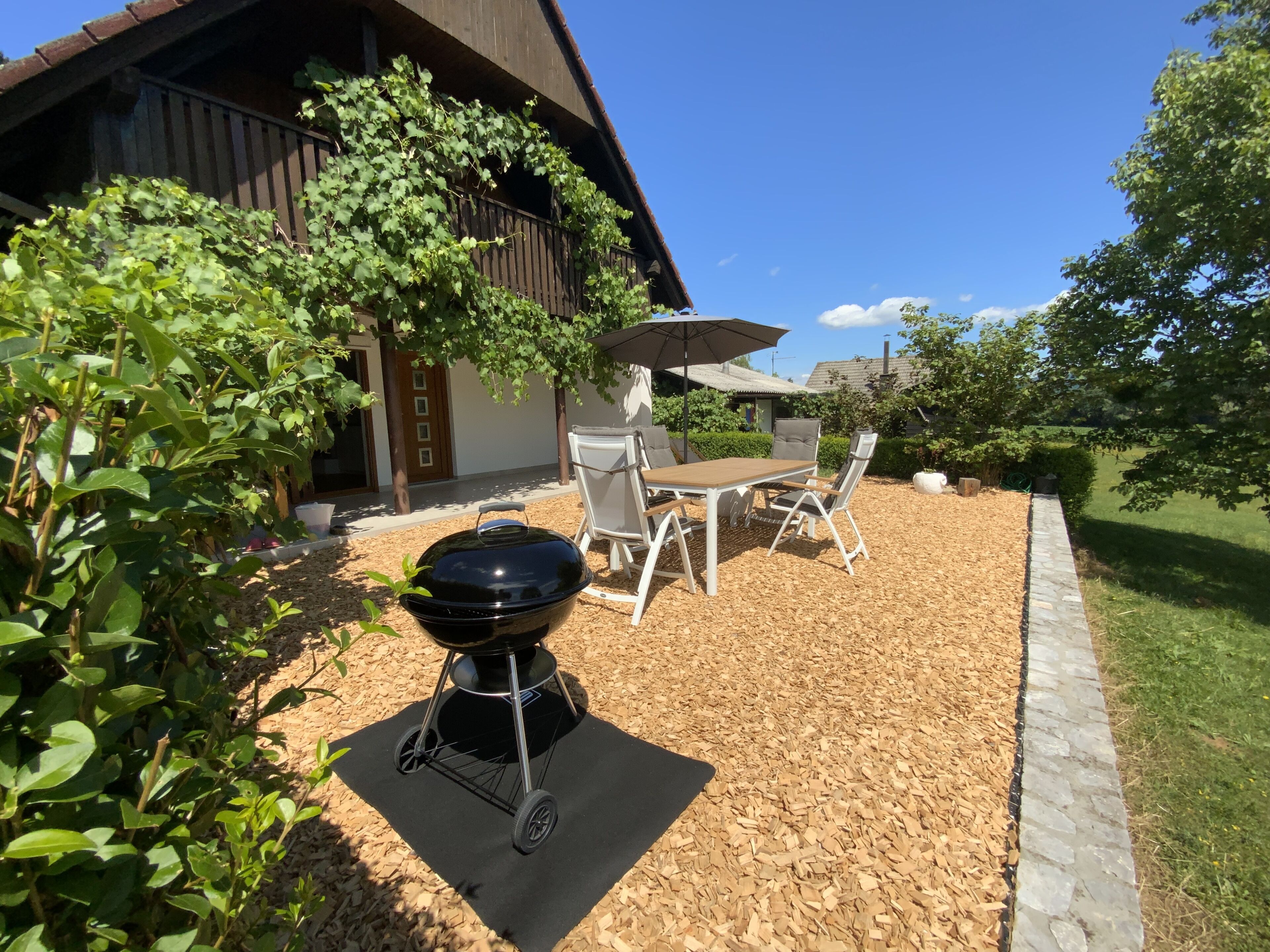 A patio area with a barbecue grill, outdoor table and chairs, and a covered umbrella.