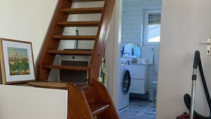 Puinen portaikko, joka johtaa pyykinpesutilaan, jossa on pesukone ja imuri.