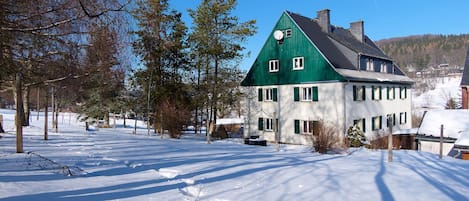 A snow-covered landscape with a green-roofed house, trees, and a clear sky.