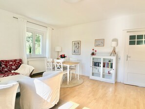A room with a sofa, a dining table with chairs, a bookshelf, and a door.