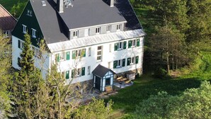 A two-story house with a sloped roof, multiple chimneys, and a large front porch with outdoor seating.