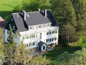 A two-story house with a sloped roof, multiple chimneys, and a large front porch with outdoor seating.