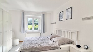 A bedroom with a bed, bedside table, lamp, clock, and a window with curtains.
