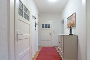 A hallway with white doors, a red carpet, and a cabinet with a picture on the wall.