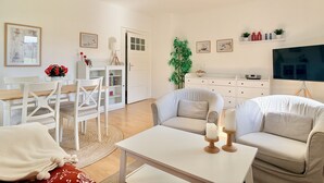 A modern living room with a sofa, a dining table with chairs, a TV, and a bookshelf.