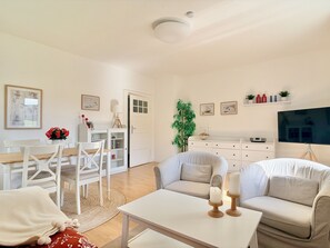 A modern living room with a sofa, a dining table with chairs, a TV, and a bookshelf.
