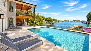 A swimming pool with lounge chairs, a wooden deck, and a view of a lake. - Lakeshore Adrift - Exclusive Lakefront Home w/Heated Pool & Custom Bunks (Denver)