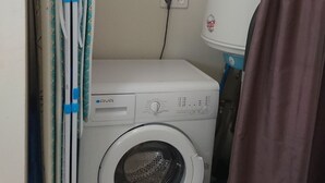 A compact laundry room with a front-loading washing machine, a drying rack, and a shelf with various items. - In the city or in the countryside! 2.7 km from the Valentré Bridge (PRADINES)