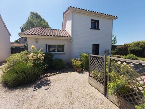 Une maison à deux étages, avec un toit recouvert de tuiles, un petit porche à l’avant et une allée gravillonnée.