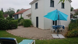 Un bâtiment blanc avec une terrasse en gravier, un parasol bleu et des sièges d’extérieur.
