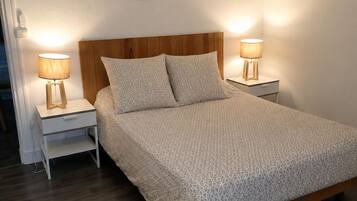 Een slaapkamer met een houten hoofdbord, twee nachtkastjes met lampen, een bed met een geborduurde spreideken en een bloemendecoratie aan de muur.