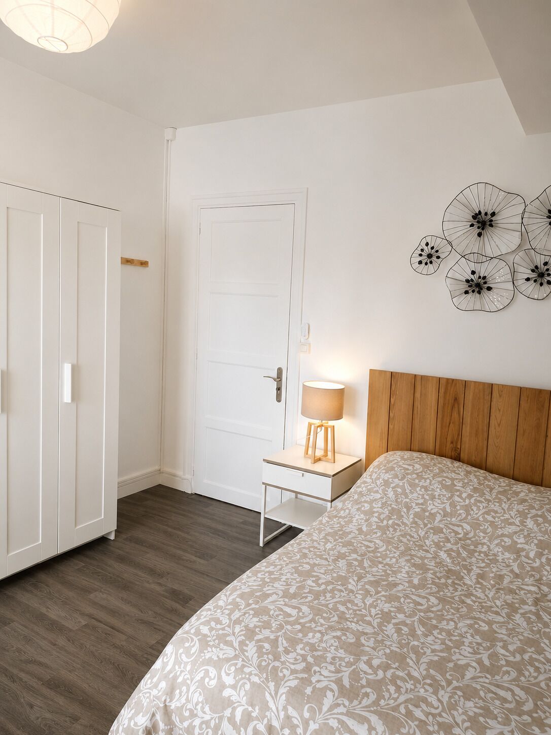 Une chambre à coucher comprenant un lit, une table de chevet avec une lampe, une armoire et une décoration florale fixée au mur.