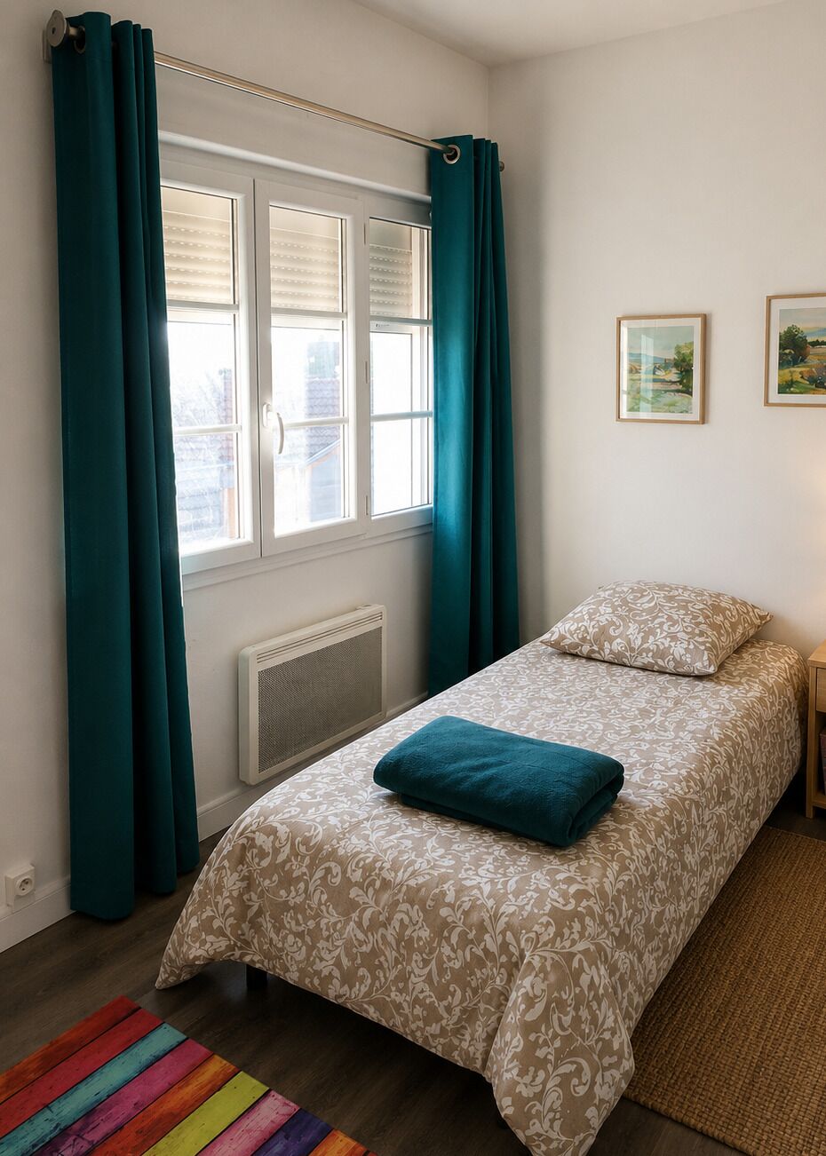 Ein Schlafzimmer mit einem Bett, blaustichigen Vorhängen, einem Heizkörper, einem Fenster mit Jalousien und zwei gerahmten Bildern an der Wand.