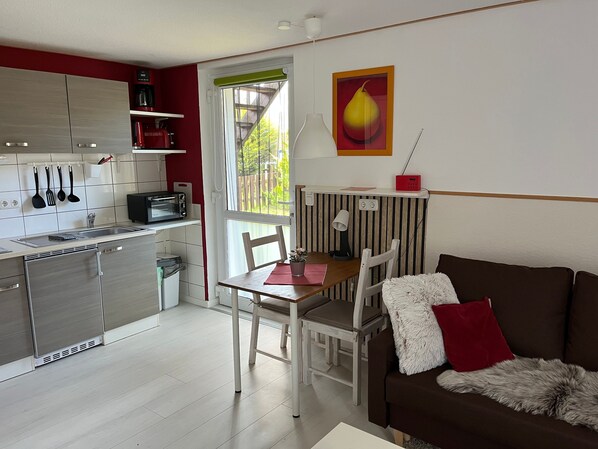 A compact kitchen with a dining area, a sofa, and a window with a view.