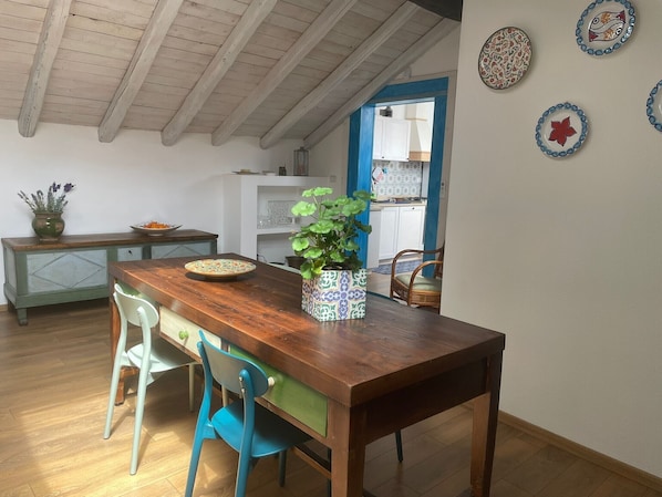 A dining area with a wooden table, two chairs, a potted plant, and a decorative plate on the wall.