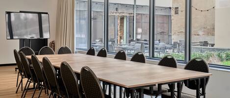 A conference room with a long table and chairs, large windows, and a TV screen.