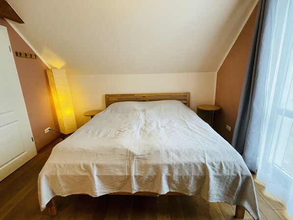 A bedroom with a wooden bed, a nightstand, a lamp, and a window with curtains. - Fewo Klein Aber Fein (Urbar)