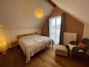 A bedroom with a wooden bed, a wicker chair, a hanging light fixture, and a window with curtains. - Fewo Klein Aber Fein (Urbar)
