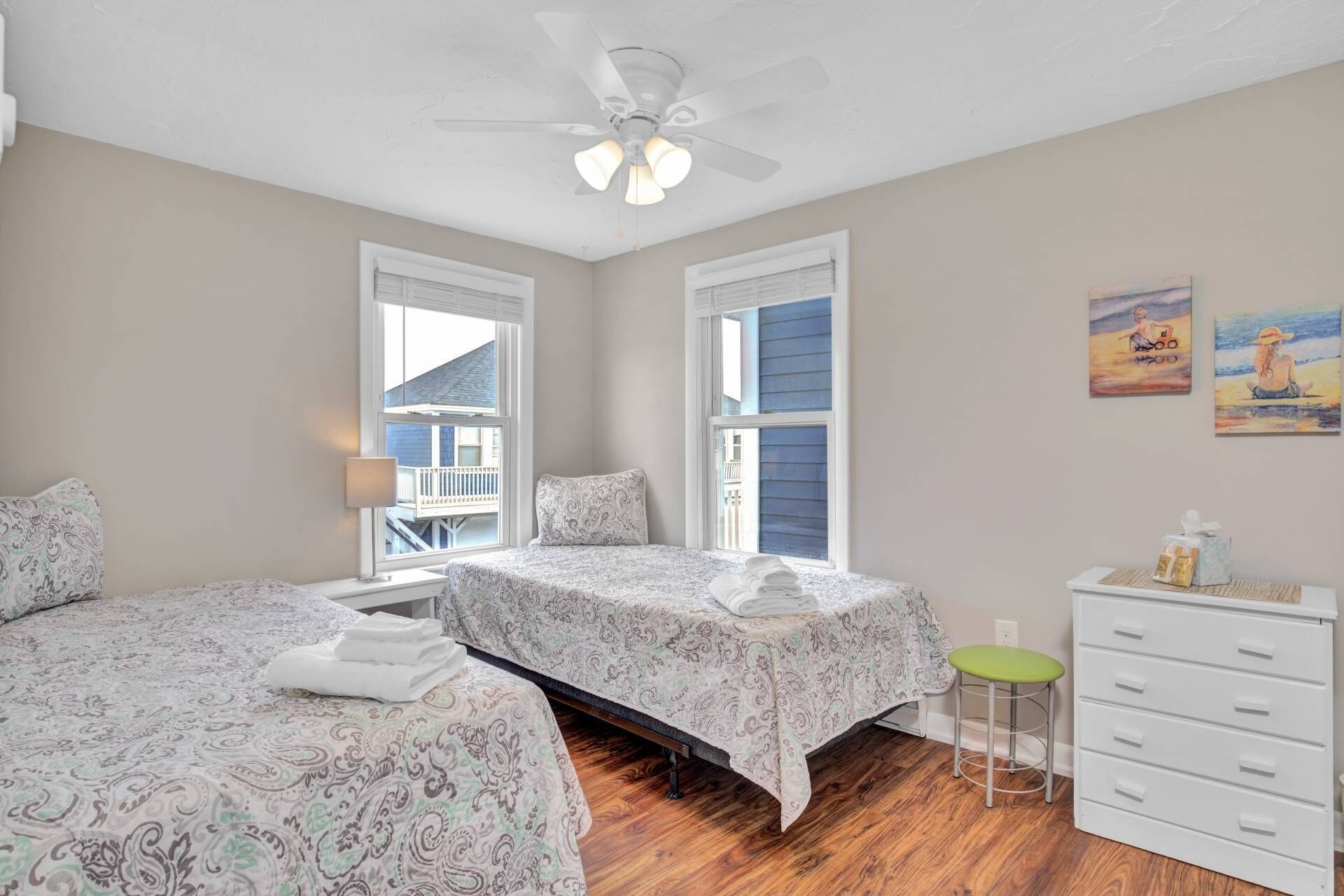 A bedroom with two beds, a ceiling fan, a window with a view, a dresser, and a chair.